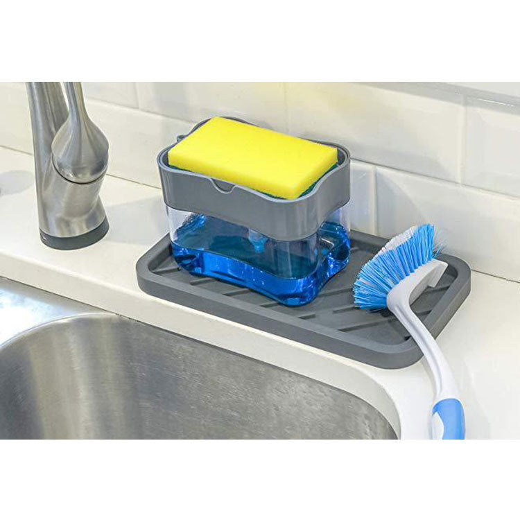 Gray dish soap dispenser holding blue liquid and a yellow sponge, pictured beside a blue-bristled dish brush on a sink-side tray.